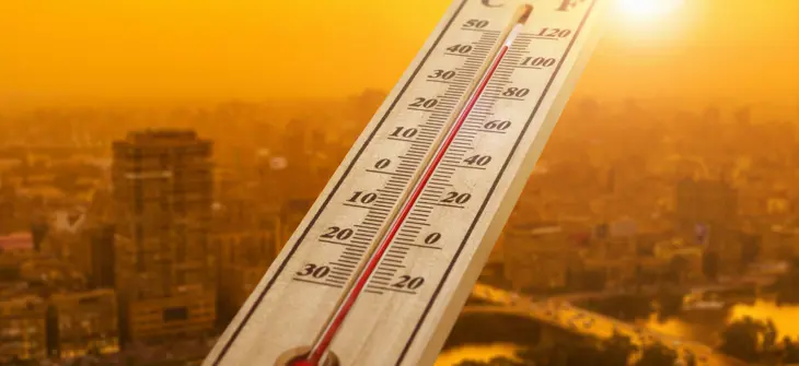 A thermometer showing high temperatures against a city skyline during a bright, sunny day.