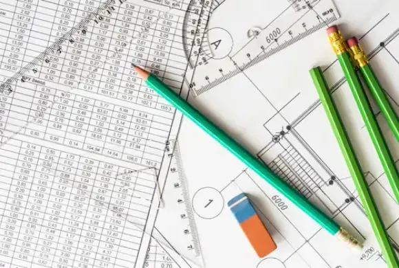 Green pencils and an eraser on top of architectural blueprints and a sheet with data tables.