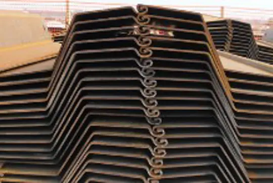 Stacked metal sheet piles arranged in a zigzag pattern at a construction site.