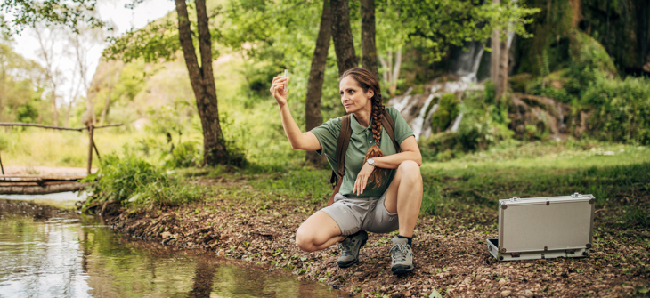 A person taking a water sample from a stream.
